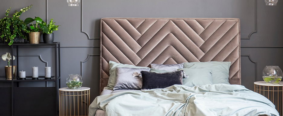 Stylish bedroom with light grey coloured walls and bed with champagne coloured velvet upholstered headboard and light grey bedding